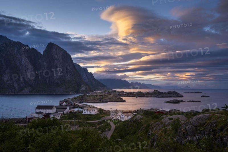 Cloudy landscape. The villages of Olenilsoy, Toppoya (Toppoy) and Hamnoy as well as the Festhaeltinden mountain. A bridge connects the islands. View across the sea towards Flakstadoya and Vestvagoya. Several coloured lenticular clouds (lenticularis) in the blue sky. At night at the time of the midnight sun. Early summer. Moskenesoya, Lofoten, Norway, Europe