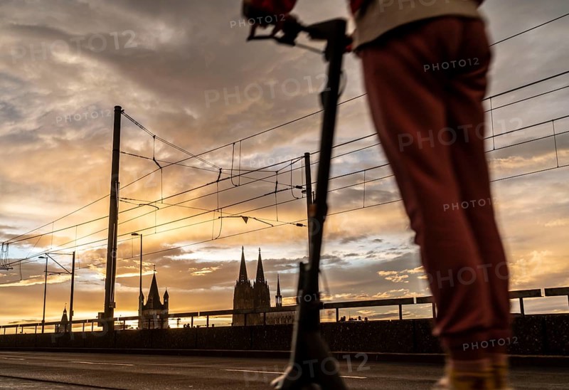 Skyline with Cologne Cathedral, Gross St. Martin Catholic Church, Deutz Bridge, sunset, e-scooter driver, Cologne, North Rhine-Westphalia, Germany, Europe