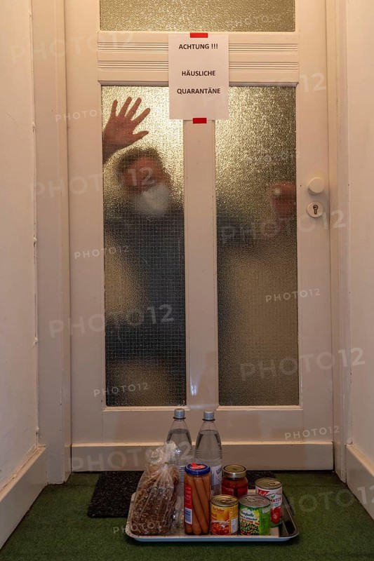 Symbolic image Domestic quarantine, man is in isolation at home due to a suspected corona infection, warning sign for visitors on the front door, communicating with a visitor through the door, neighbours have placed food in front of the door