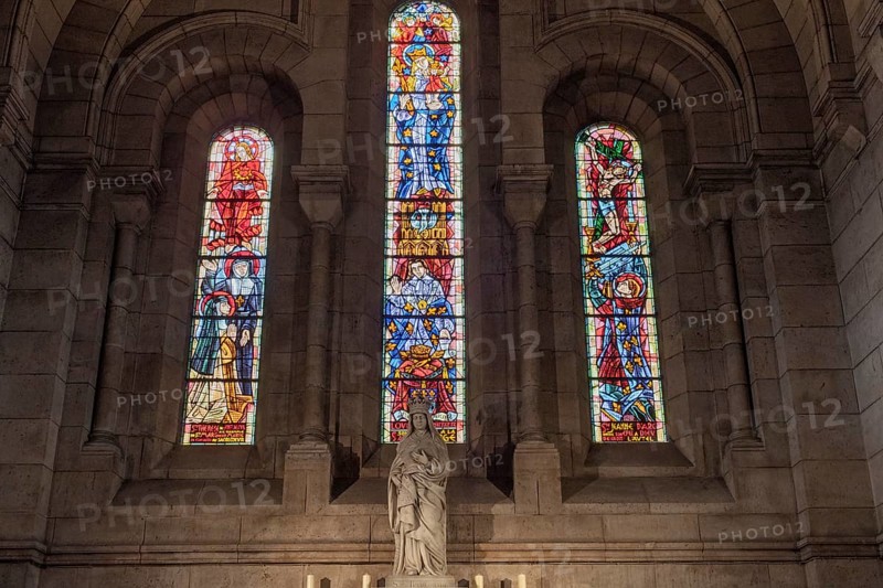 Stained glass windows illuminate a statue in a church, warm light floods in, Paris