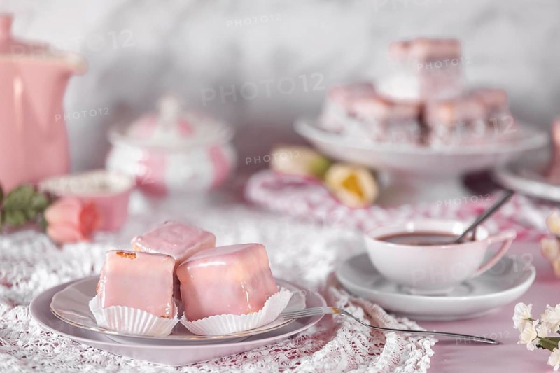 Pink glazed cakes, punch doughnuts and a coffee cup on a table decorated with flowers
