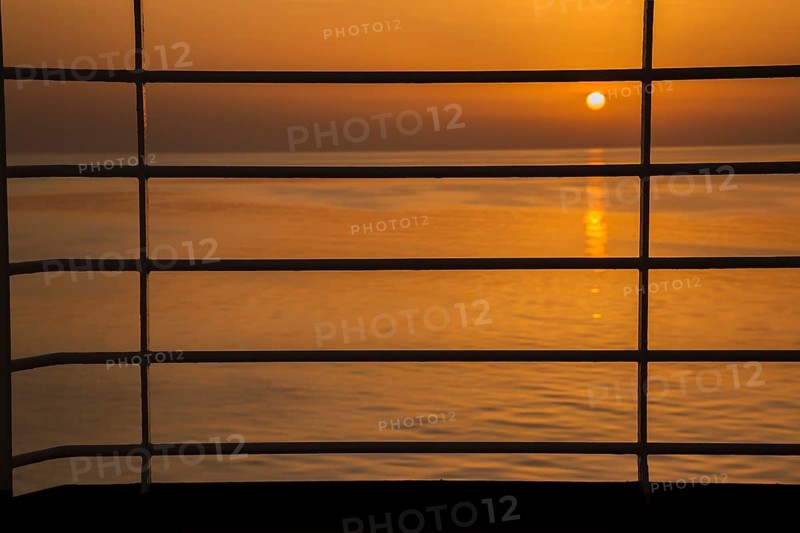 Close-up of silhouetted railing on cruise ship and golden setting sun over Adriatic sea near Zadar, Croatia in summer