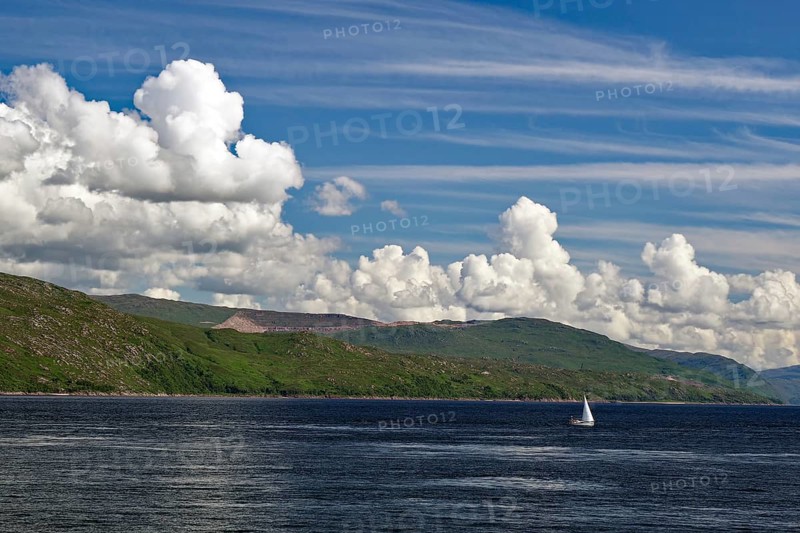 Single sailing boat on the sea, surrounded by a mountain landscape, under a sky with many clouds, ferry Oban, Mull, Scotland, Great Britain