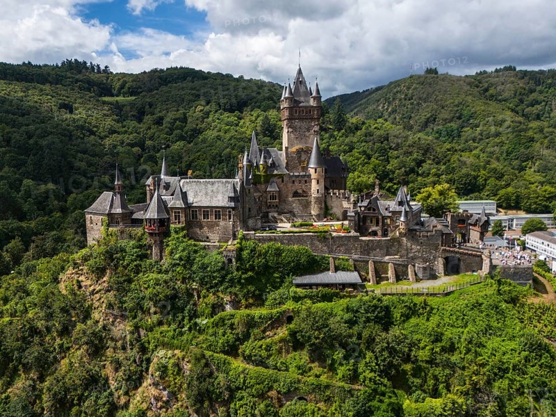A historic castle on a green, wooded hill under a cloudy sky, aerial view, Reichsburg, Cochem, Cochem-Zell, Moselle, Rhineland-Palatinate, Germany, Europe