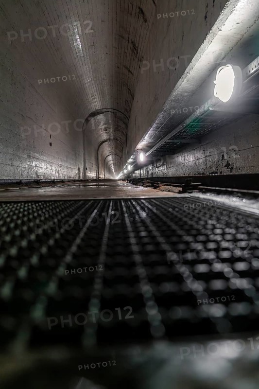 Long concrete tunnel with grid floor and damp surfaces, illuminated by lamps on the sides, Rappbode Dam, Harz Mountains, Germany, Europe