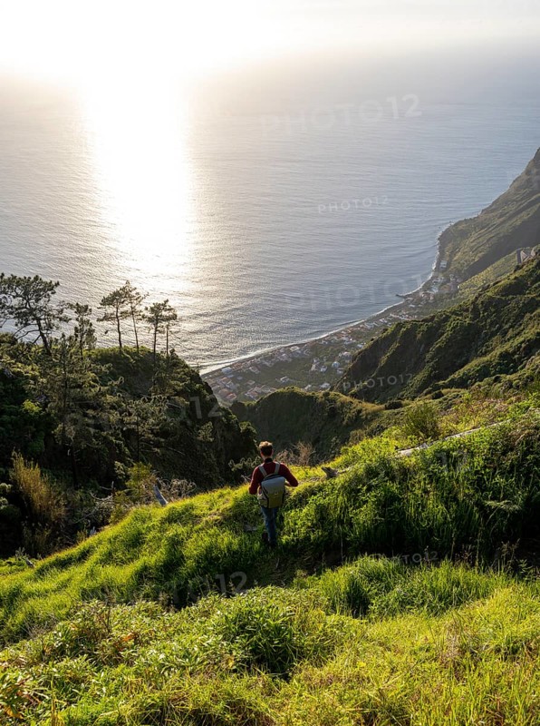Young man looking out to sea on cliff, evening mood, green coastal landscape on cliff, sea and coast, viewpoint Miradouro da Raposeira, Paul do Mar, Madeira, Portugal, Europe