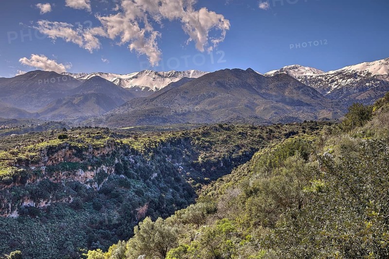 Green gorge with lush vegetation framed by snow-capped mountains and a blue sky with clouds, Lefka Ori, White Mountains, mountain massif, West, Crete, Greece, Europe