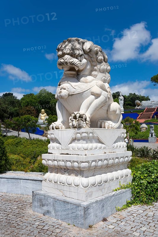 A stone lion statue on a pedestal, surrounded by plants under a blue sky with clouds, Bacalhôa, Bacalhoa Buddha Eden, Quinta dos Loridos, largest oriental garden in Europe, Bombarral, Oeste, Centro, Portugal, Europe