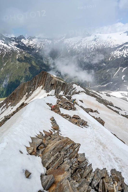Mountaineer on a rocky ridge with snow, descent from the summit of Schönbichler Horn, view of snow-covered mountain peaks and valley Zemmgrund, Berliner Höhenweg, Zillertal Alps, Tyrol, Austria, Europe