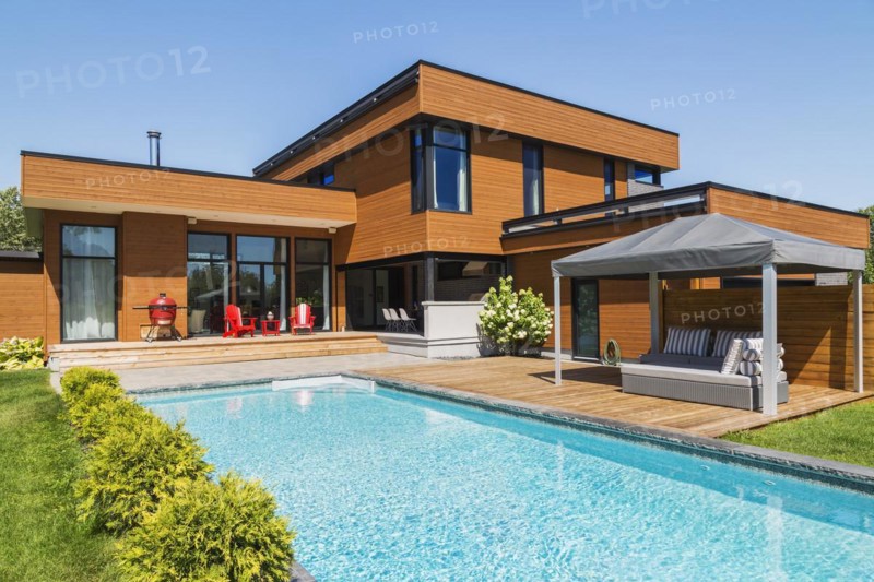 Rear of modern cube style home with stained horizontal wood cladding, in-ground swimming pool and wooden deck with grey gazebo canopy, Quebec, Canada, North America