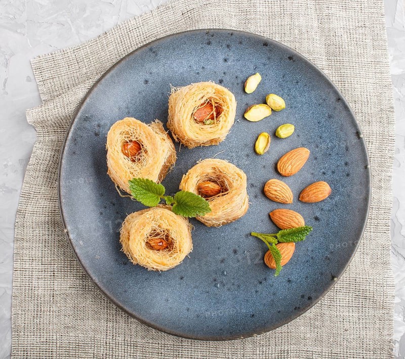 Kunafa, traditional arabic sweets in blue ceramic plate on a gray concrete background. top view, close up