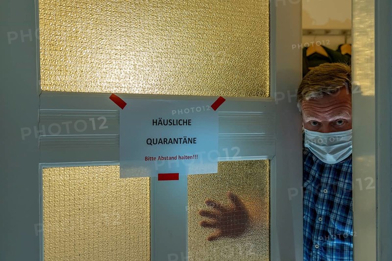 Symbolic image Domestic quarantine, man is in isolation at home due to a suspected corona infection, warning sign for visitors on the front door, communicating with a visitor through the door