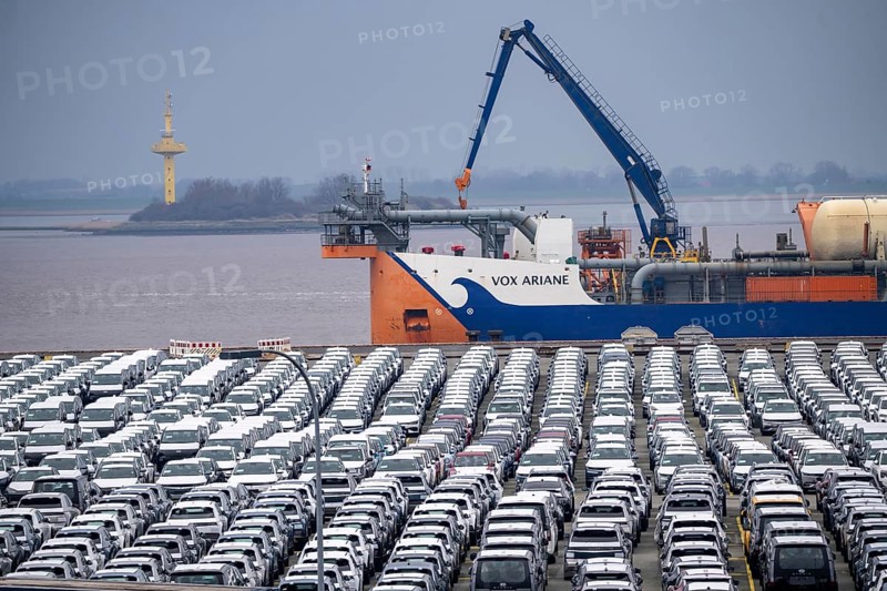 Parking space for import vehicles, hundreds of Hyundai Ioniq, electric cars, waiting for onward transport, behind them, on the Weser, the dredger, the hopper dredger, suction dredger, Vox Ariane, which holds the tug to a certain depth, at the EUROGATE container terminal in the overseas port of Bremerhaven, Lower Saxony, Germany, Europe