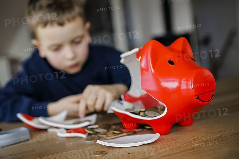 Symbolic photo on the subject of saving. A boy smashes his savings slip and counts the money it contains. Berlin, 10.02.2024