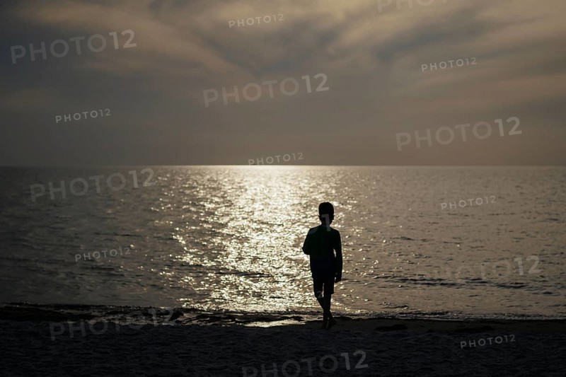 A child stands alone on the beach in the backlight of the setting sun. Born, 01.08.2024