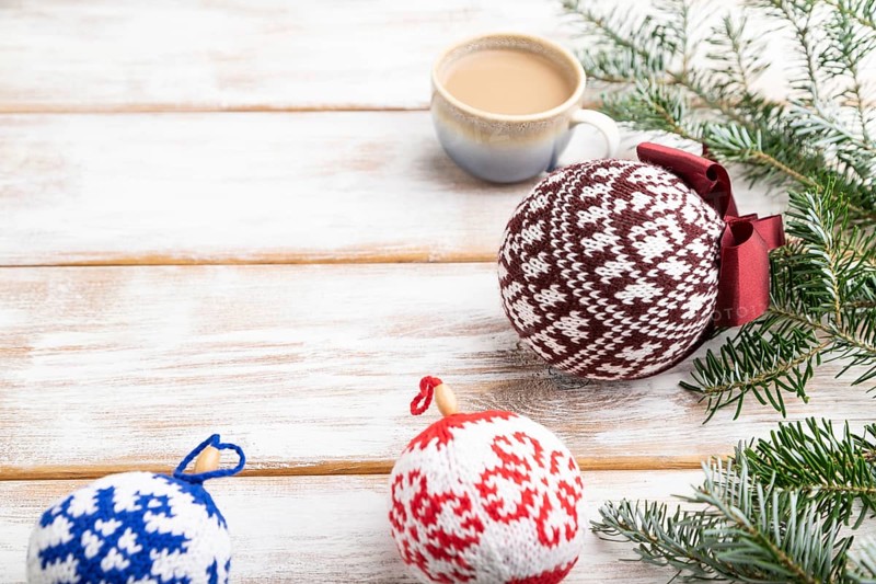 Christmas or New Year composition. Decorations, knitted balls, fir and spruce branches, cup of coffee, on a white wooden background. Side view, copy space, selective focus