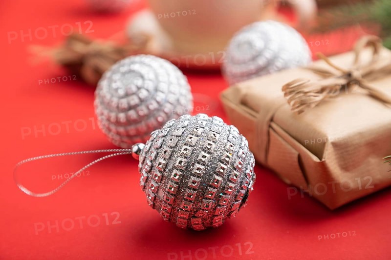 Christmas or New Year composition. Decorations, box, cinnamon, silver balls, fir and spruce branches, cup of coffee, on a red paper background. Side view, close up, selective focus