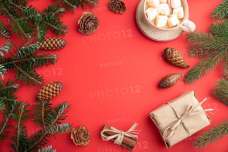 Christmas or New Year frame composition. Decorations, box, cinnamon, cones, fir and spruce branches, cup of coffee, on a red paper background. Top view, copy space, flat lay