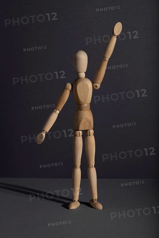 Wooden mannequin stands with raised hand on gray background. protest, attention concept. copy space, hard light