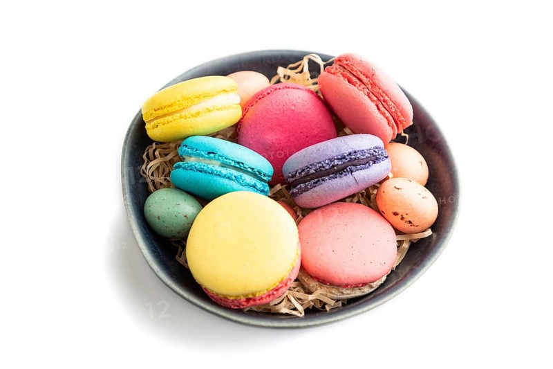 Multicolored macaroons and chocolate eggs in blue ceramic bowl isolated on white background. side view, close up, still life. Breakfast, morning, concept