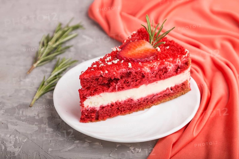 Homemade red velvet cake with milk cream and strawberry on a gray concrete background with red textile. side view, close up, selective focus