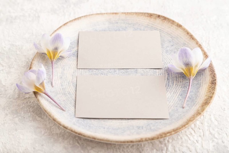 Gray paper invitation card, mockup with crocus flowers on ceramic plate and gray concrete background. Blank, flat lay, top view, still life, copy space, wedding invitation