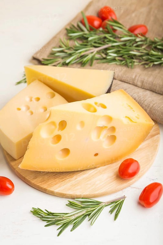 Various types of cheese with rosemary and tomatoes on wooden board on a white wooden background and linen textile. Side view, close up, selective focus