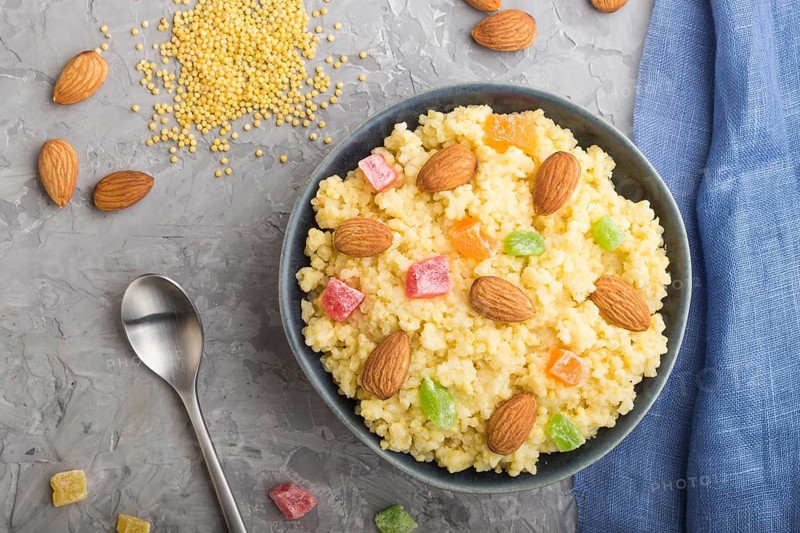 Millet porridge with candied fruits and almonds in blue ceramic bowl on a gray concrete background and blue linen textile. Top view, flat lay, close up