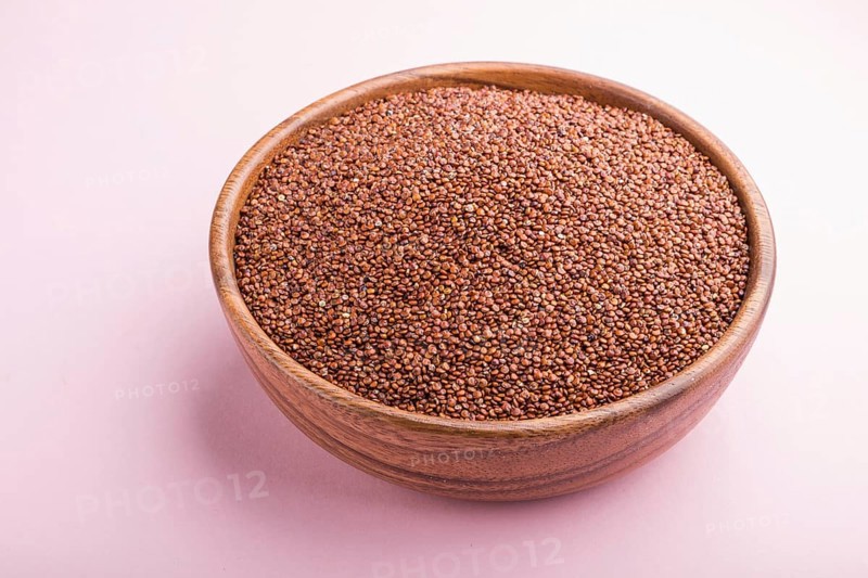 Wooden bowl with raw red quinoa seeds on a pastel pink background. Side view, close up