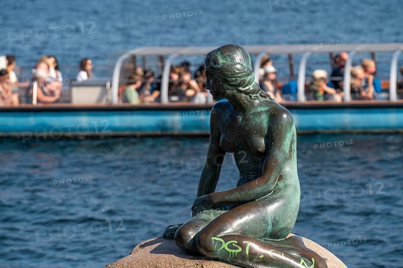The Little Mermaid statue, Den lille Havfrue in Danish, on the Langelinie waterfront promenade in Copenhagen, is considered the smallest landmark in the world, bronze figure on a boulder, tourists in a tour boat, Copenhagen Denmark