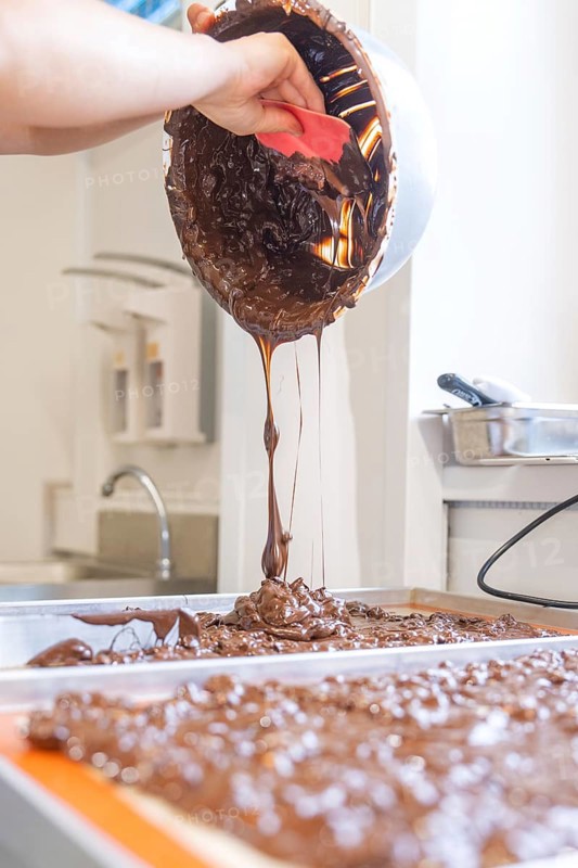 A hand pours liquid chocolate from a bowl onto a surface, Burch Schokolade production, Haselstaller Hof, Gechingen, Germany, Europe