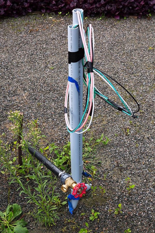 Close-up of newly installed black plastic garden hose main water supply connecting pipe with brass fitting and red tap plus unfinished electrical installation in public garden park in summer, Quebec, Canada, North America