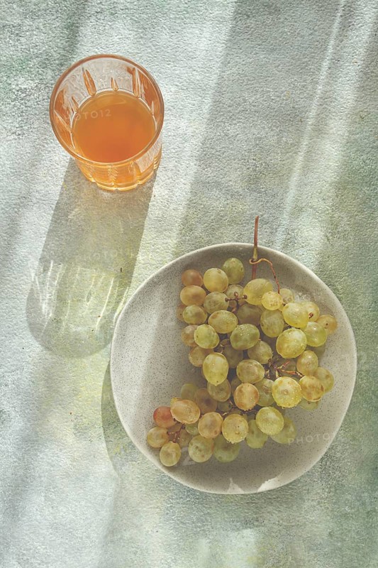 A branch of white grapes, on a gray plate, with a glass of white wine, top view, natural light, food concept, no people