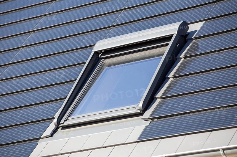 Roof window on a detached house with solar roof tiles. Solar tiles are a beautiful and high-quality alternative to conventional photovoltaic systems