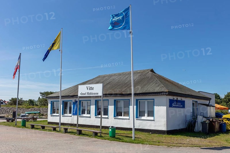 Small historic building with waving flags under a blue sky in sunny weather, Rügen, Hiddensee