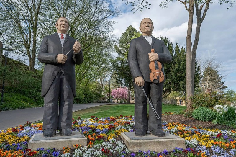 Statues of two men, one with a violin, the other with a conductor's baton, stand in a colourful garden in spring, sculptures in Siegen