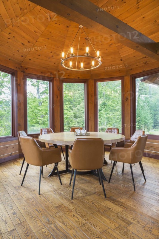 Round wooden dining table with tan leather armchairs in dining room inside a milled Eastern white pine timber and flat log profile home, Quebec, Canada, North America