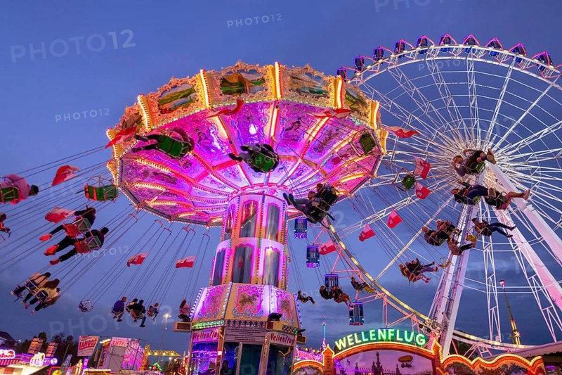 A lively funfair at dusk, illuminated by a large Ferris wheel and a colourful chain carousel, Cannstadter Volksfest, Stuttgart-Bad Cannstadt, Baden-Württemberg