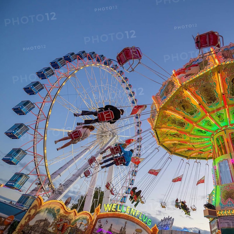 A funfair at dusk with illuminated chain carousel and Ferris wheel, Europa Rad, rides, wave flight, Cannstatter Wasen, folk festival, Bad Cannstatt, Stuttgart, Baden-Württemberg, Germany, Europe
