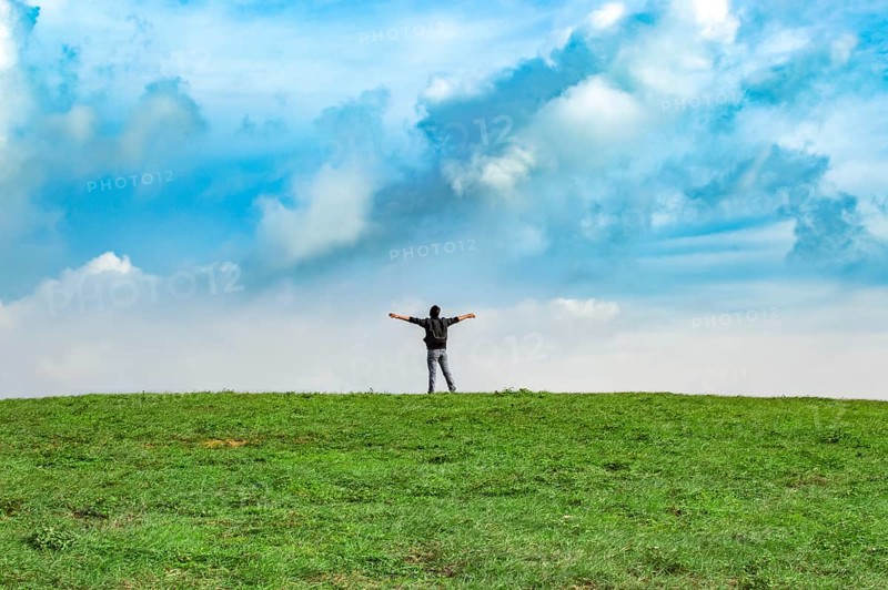 View of a backpacker man spreading his arms on a hill. Successful backpacker on top of a hill