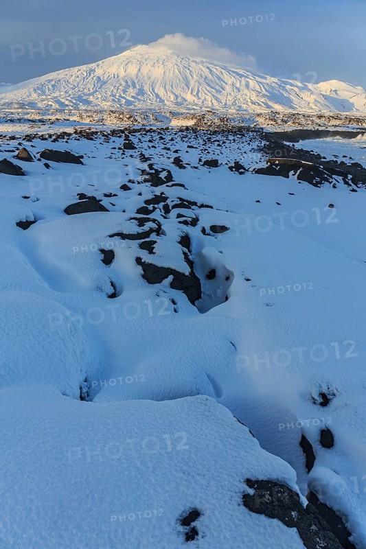 Lava field in front of a volcano, evening light, sun, snow, winter, Arnarstapi, Snaefellsjökull, Snaefellsnes, Vesturland, Iceland, Europe
