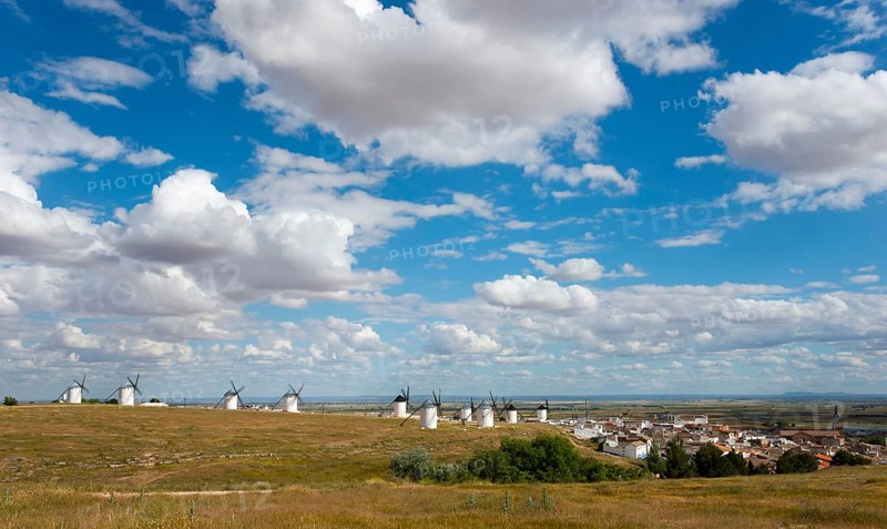 Wide landscape with windmills and a village in the background. The sky is blue with many white clouds and the surroundings are green and extensive, windmills and village, Campo de Criptana, Ciudad Real province, Castilla-La Mancha, Route of Don Quixote, Spain, Europe
