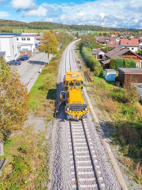 Yellow vehicle on ballast track in residential area under blue sky with clouds, tamping machine, Hermann Hessebahn, Althengstett, Black Forest, Germany, Europe