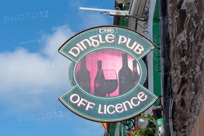 Traditional Dingle pub sign with wine bottles and glass attached to a stone façade under a blue sky, Dingle, Dingle Peninsula, County Kerry, Republic of Ireland