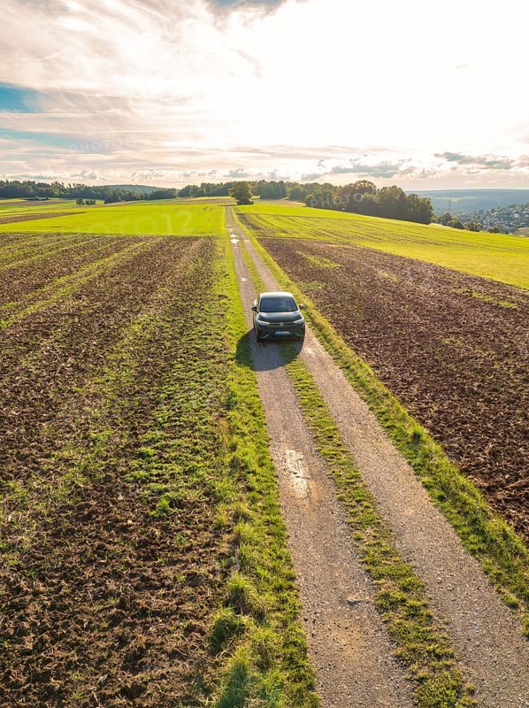 Black car driving on a narrow country lane through wide fields under a cloudy sky, Carsharing, VW ID5, Calw, Black Forest, Germany, Europe