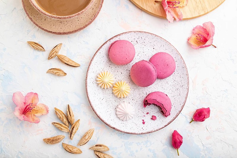 Purple macarons or macaroons cakes with cup of coffee on a white concrete background decorated with flowers. Top view, flat lay, close up