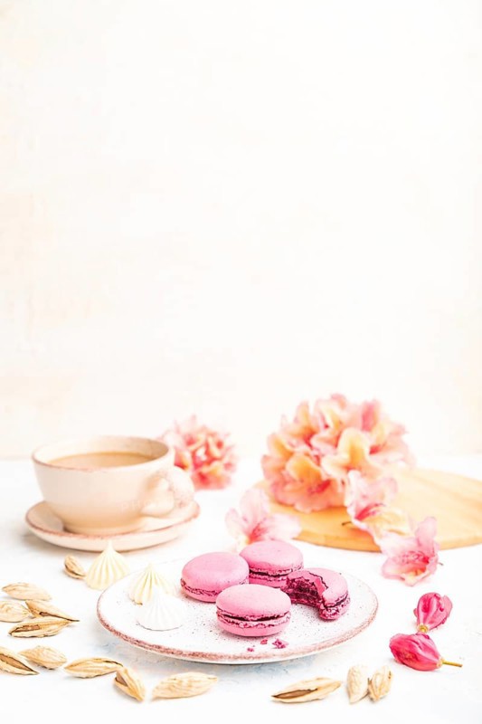 Purple macarons or macaroons cakes with cup of coffee on a white concrete background decorated with flowers. Side view, copy space, selective focus