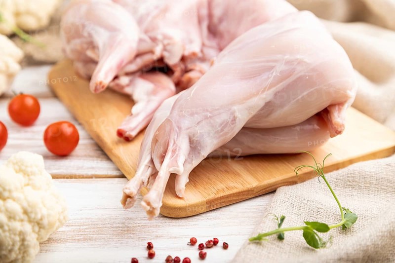 Whole raw rabbit with cauliflower, tomatoes and spices on a white wooden background and linen textile. Side view, close up, selective focus