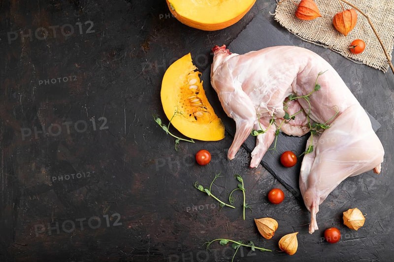 Whole raw rabbit with pumpkin, tomatoes, pea sprouts on a black concrete background and linen textile. Top view, flat lay, copy space