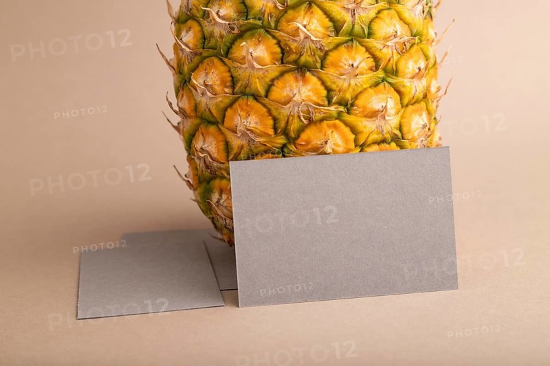 Gray paper business card with ripe pineapple on orange pastel background. Side view, copy space. Tropical, healthy food, vacation, holidays concept